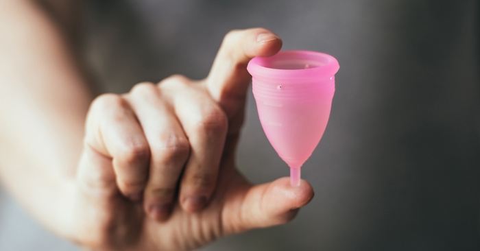 Young woman hand holding menstrual cup. Selective focus and shallow DOF; blog: menstrual cup pros and cons
