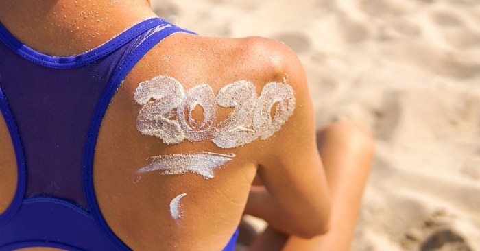 Christmas time spent at the beach in summer. Young woman wearing sunscreen that spells 2020; blog: 8 Healthy Habits for the New Year