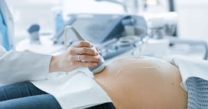 In the Hospital, Close-up Shot of the Doctor Doing Ultrasound / Sonogram Scan to a Pregnant Woman. Obstetrician Moving Transducer on the Belly of the Future Mother; High-Risk Obstetrics
