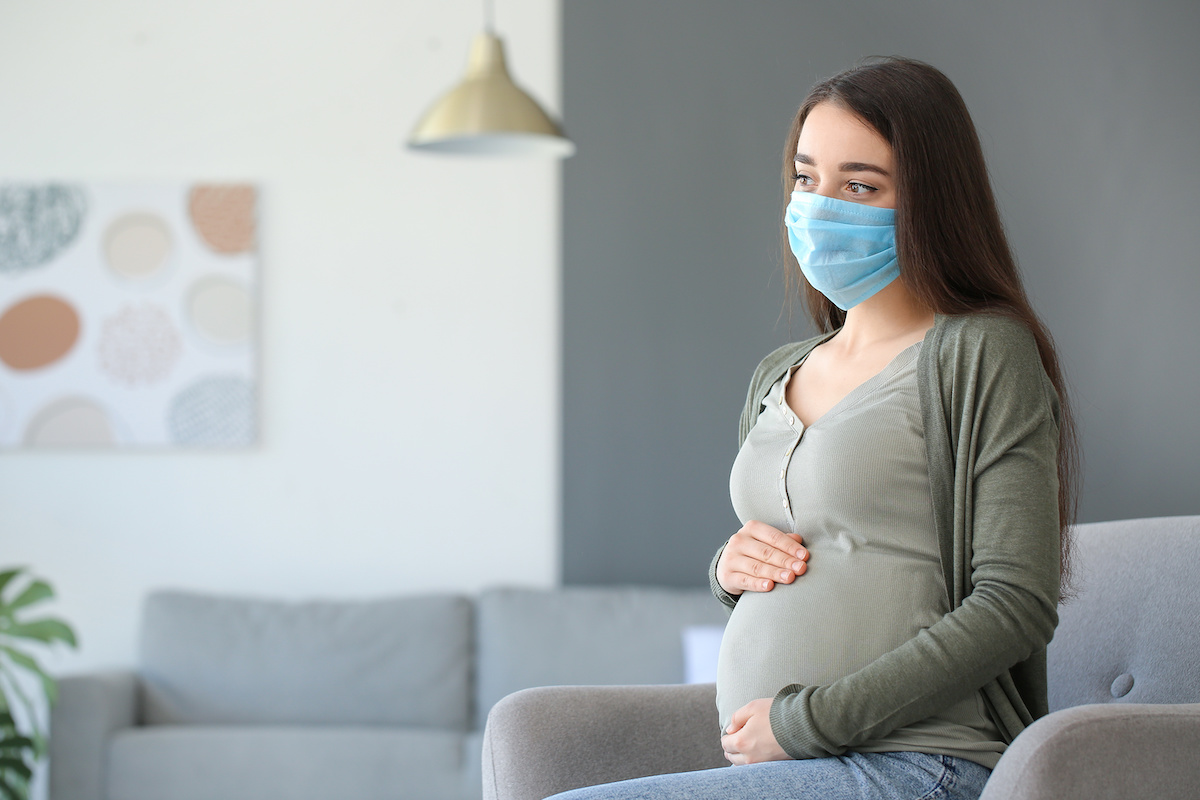 Pregnant woman wearing medical mask at home; blog: Pregnancy, Anxiety and the Pandemic